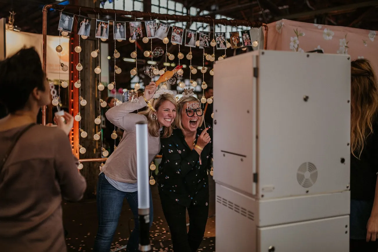 Zwei Frauen lachen ausgelassen vor der SNAPSHOT2GO Fotobox bei einer Feier mit Konfetti und Party-Accessoires